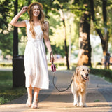 Woman in a white dress walking a dog on a leash in a park.